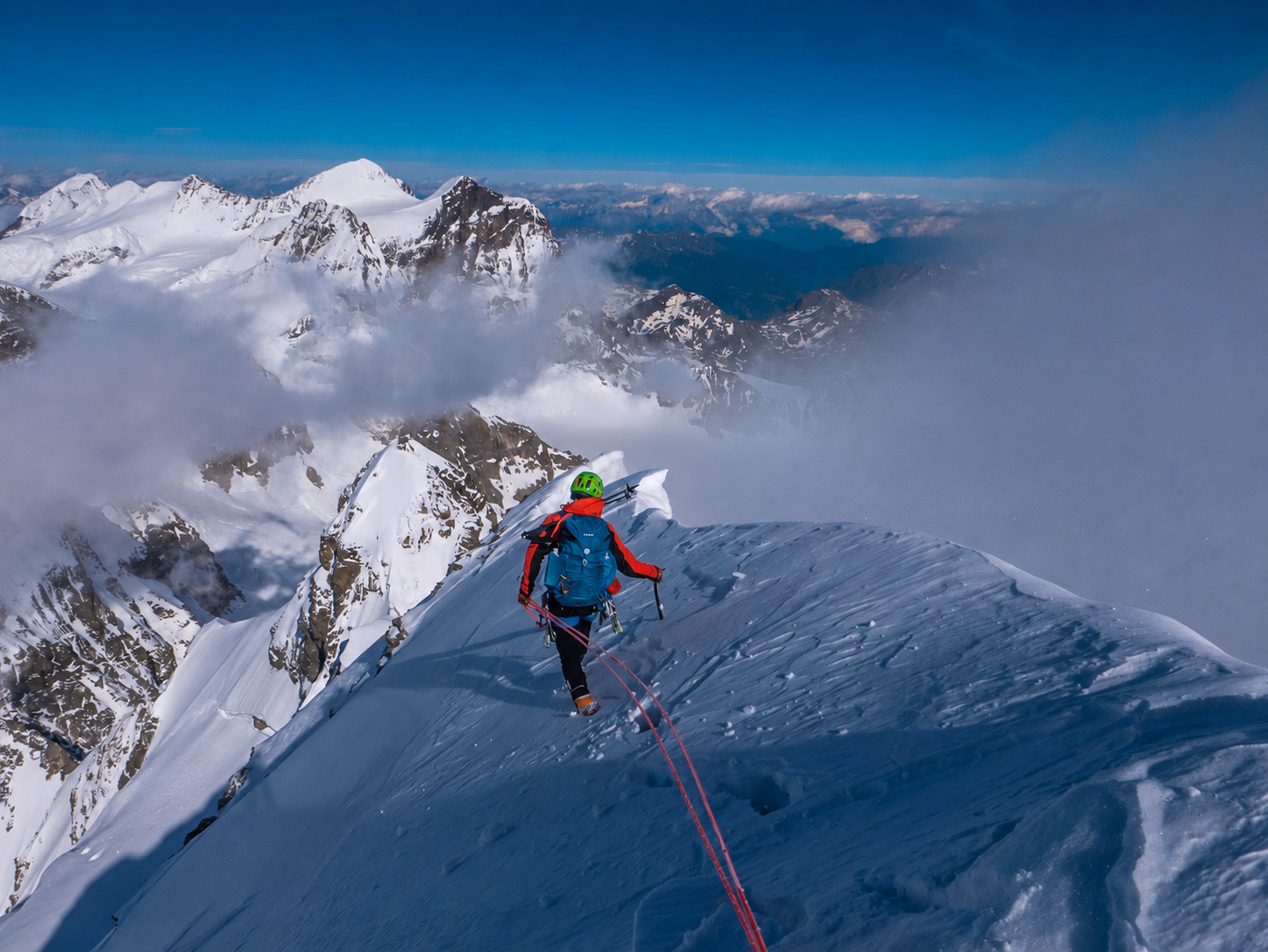 Alpiniste encordé sur une arête de neige au-dessus d’une mer de nuages